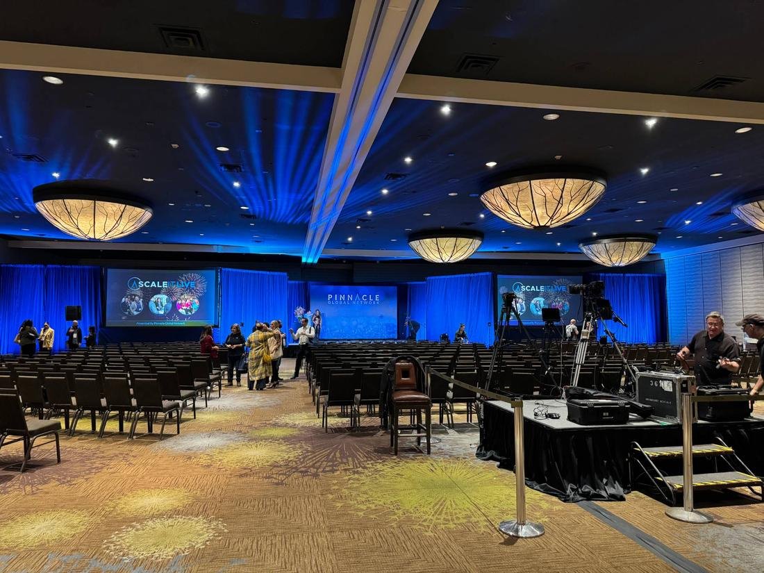 Large ballroom with blue light beams across the ceiling, blue draped walls, screens and rows of chairs