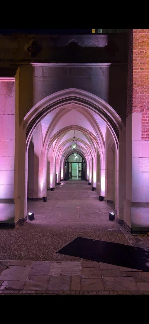 Stone arched walkway at night lit with soft pink uplights placed along the columns