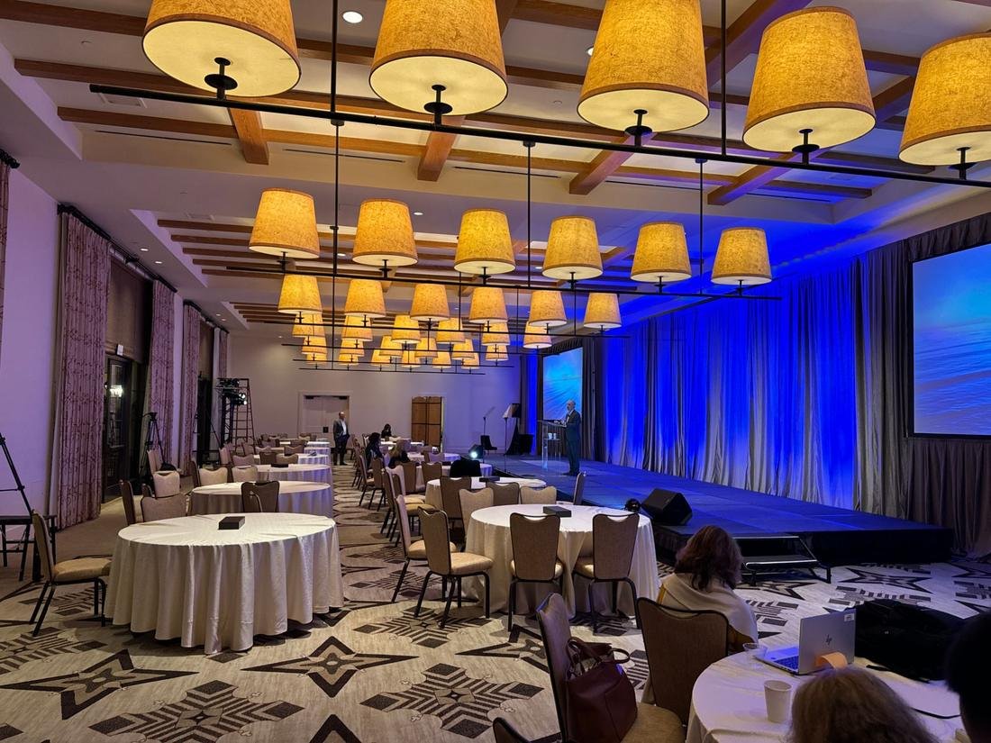 Event room with a stage and draped walls uplit in deep blue under large hanging lamp shades