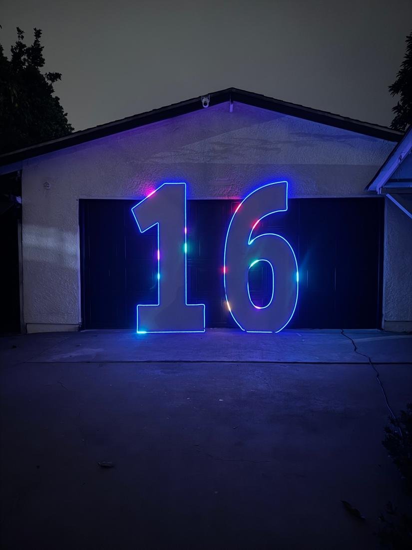 Giant marquee number 16 outlined in blue LED with color chasing pixels in front of a garage